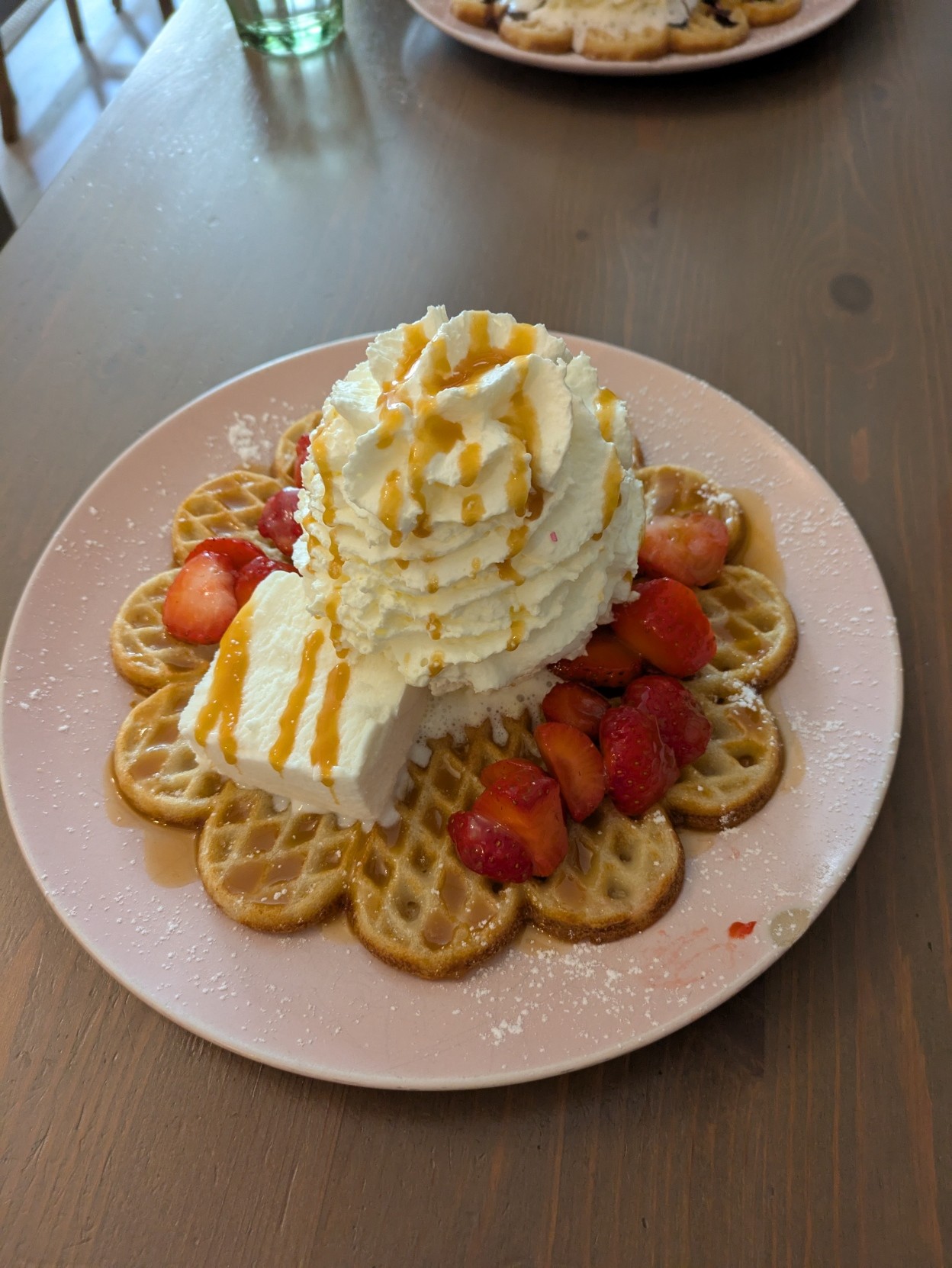 A waffle with a piece of vanilla ice cream, a huge pile of whipped cream, caramel sauce and fresh strawberries on top of it.